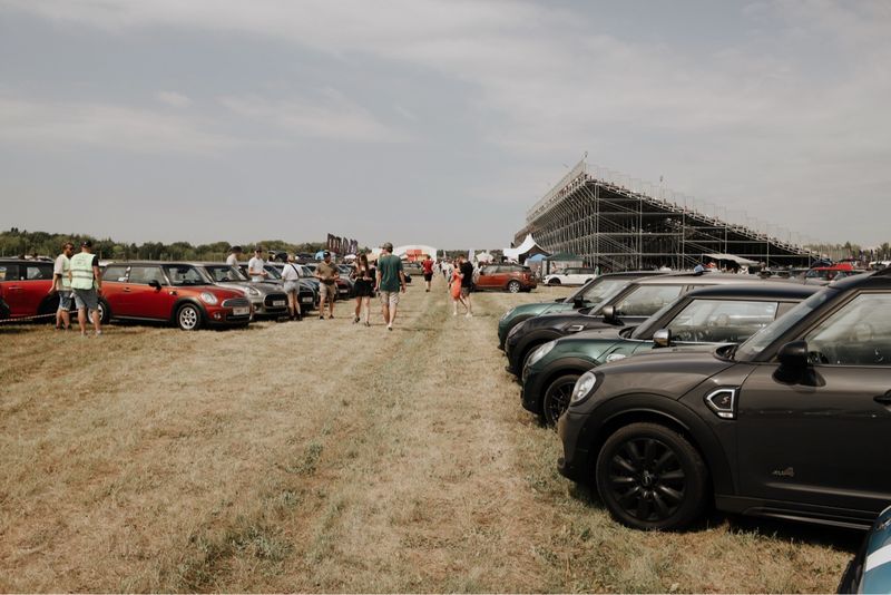 Люди идут между припаркованными MINI у трибуны — Not Normal Camp 2024